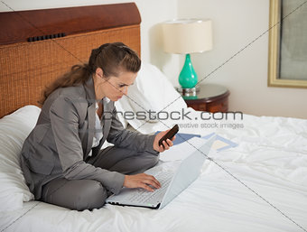 Business woman working with documents on bed in hotel room