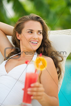 Happy young woman with cocktail laying on chaise-longue