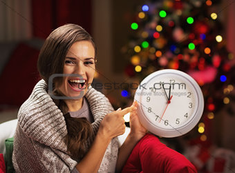 Smiling young woman near christmas tree pointing on clock