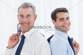 Smiling businessmen posing back to back together while holding their jacket