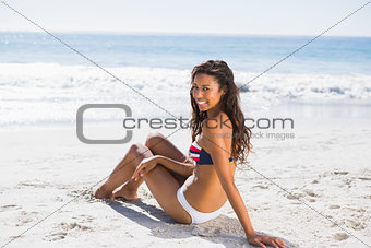 Sexy tanned woman in bikini looking at camera while sitting