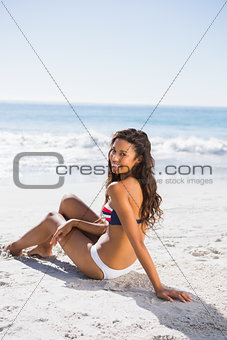 Sexy tanned woman in bikini smiling at camera while sitting