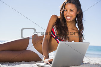 Happy sexy young woman in bikini using her laptop