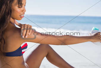 Sexy woman in bikini applying sun cream on her shoulder