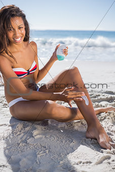 Smiling woman applying sun cream on her leg