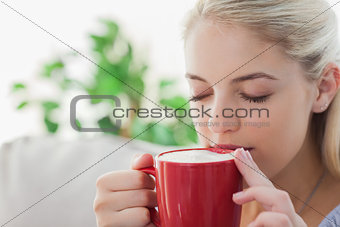 Blonde woman holding a red mug and sipping from it