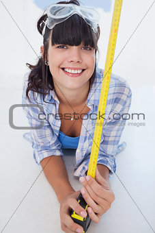 Happy woman lying on floor with measuring tape and safety goggles