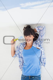 Attractive woman lying on floor holding paint brush overhead