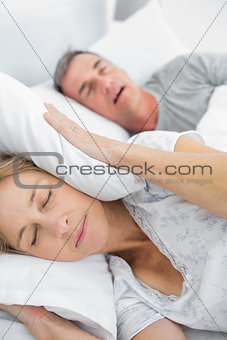 Tired wife blocking her ears from noise of husband snoring