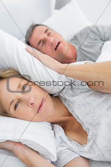 Tired wife blocking her ears from noise of husband snoring looking at camera