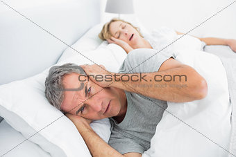 Annoyed man blocking his ears from noise of wife snoring