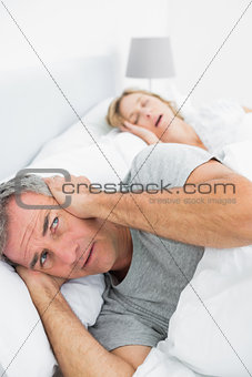 Irritated man blocking his ears from noise of wife snoring