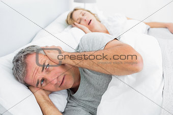 Fed up man blocking his ears from noise of wife snoring