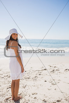 Brunette in white sunhat and dress looking over her shoulder at camera