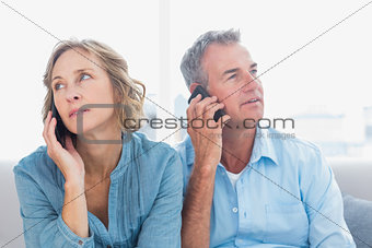 Unsmiling couple on their mobile phones on the couch