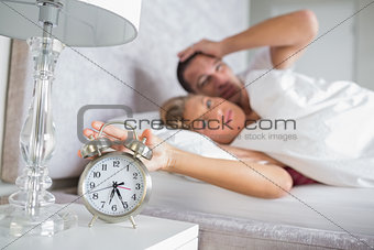 Tired couple looking at alarm clock in the morning with woman turning it off