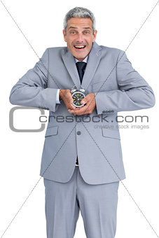 Cheerful businessman with alarm clock in both hands