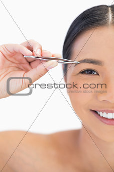 Half face of smiling natural woman using tweezers