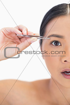 Half face of surprised natural woman using tweezers