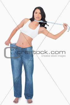 Sexy woman wearing too big pants and strangling herself with measuring tape