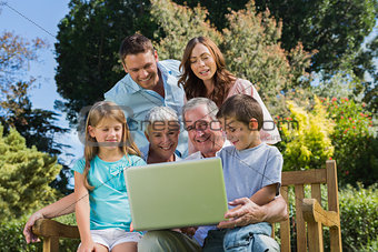 Smiling multi generation family with a laptop sitting in park