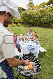 Smiling extended family having a barbecue being cooked by father in chefs hat
