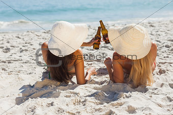 Attractive blonde and brunette in bikinis clinking glass bottles