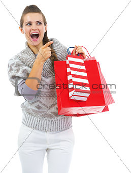 Surprised young woman in sweater with shopping bags pointing on 