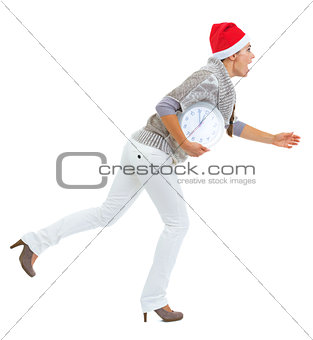 Shocked young woman in sweater and christmas hat running with cl