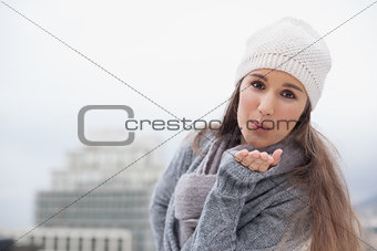 Pretty brunette with winter clothes on sending an air kiss to camera