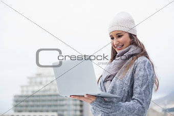 Cheerful woman with winter clothes on using her laptop