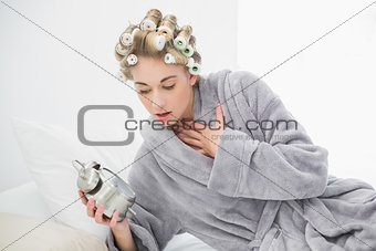 Stressed blonde woman in hair curlers looking at her alarm clock