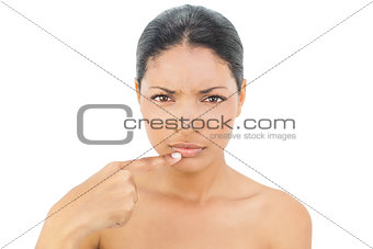 Frowning black haired model pointing at her bottom lip