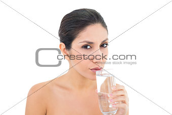 Happy brunette sipping glass of water and looking at camera