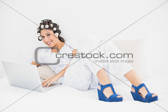 Brunette in hair rollers and wedge shoes using her laptop on bed