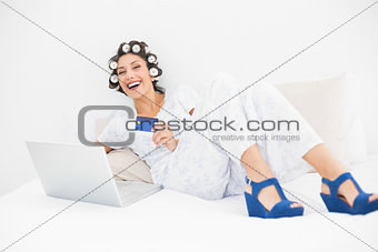Brunette in hair rollers and wedge shoes using her laptop to shop online