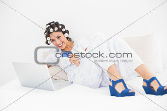 Brunette in hair rollers and wedge shoes using her laptop for shopping online