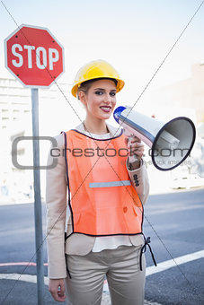 Smiling businesswoman wearing builders clothes shouting in megaphone