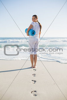 Rear view of gorgeous woman holding exercise mat looking over shoulder at camera