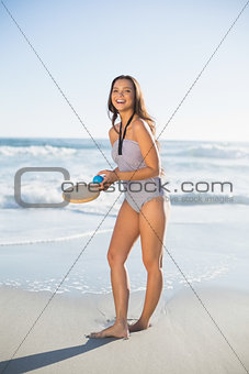 Smiling woman in one piece swimsuit playing with beach racket