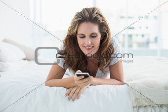 Smiling woman resting in bed text messaging
