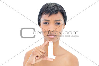 Frowning black haired woman holding an asthma inhaler