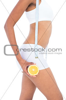 Close up of a fit woman wearing a tape measure around her neck and holding half an orange