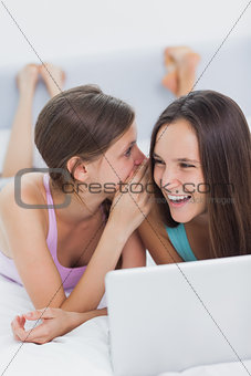 Happy girls lying in bed with laptop