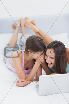 Friends lying in bed in pajamas with laptop