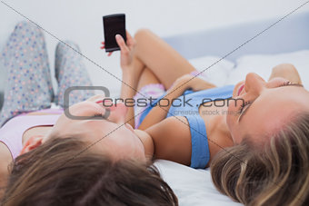 Smiling girls lying on bed using phone