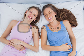 Smiling friends lying in bed and looking at camera