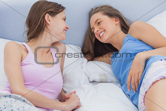 Happy friends resting in bed and talking