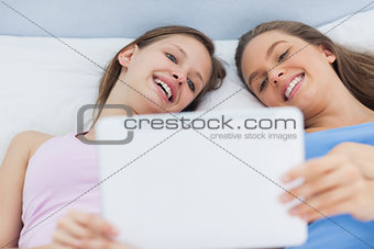Happy girls lying in bed holding tablet