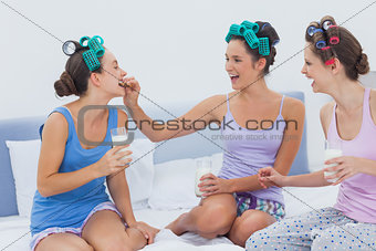 Laughing friends sitting in bed having milk and cookies